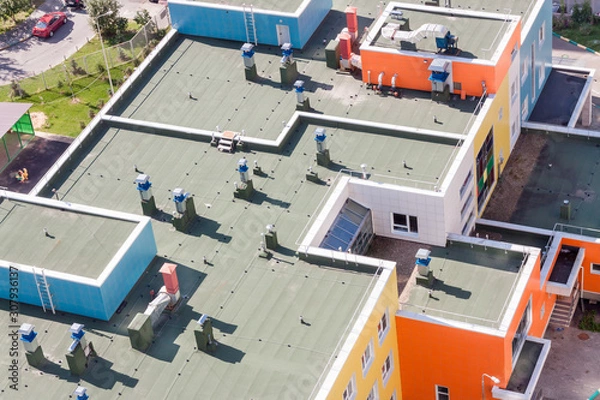 Fototapeta Top view flat roof with air conditioners and hydro insulation membranes on top of a modern blue and orange apartment building sunny summer day.