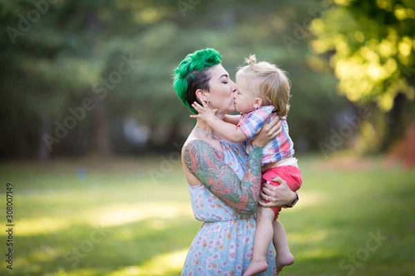 Fototapeta A portrait of Caucasian young woman with green hair and tattoo holding a blond toddler boy in her hands. Hugging, Mother's day concept