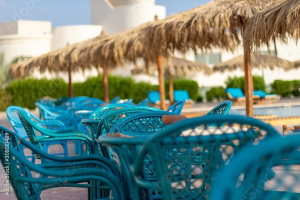 Fototapeta Turquoise rattan furniture by the pool on a sunny morning.