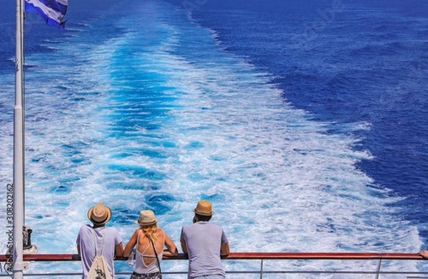 Fototapeta Tourists with a straw hat stand on the deck of a cruise ship and look out over the ocean  While the boat is sailing.