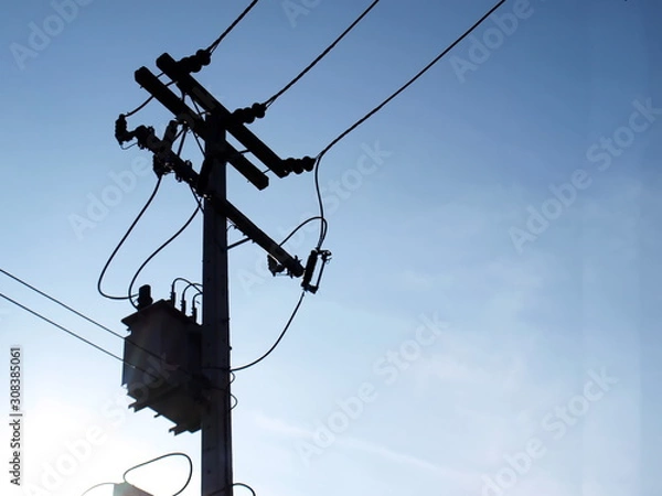 Fototapeta Silhouettes of power transformers and high-voltage wires on a pole. On the blue sky background and copy space.