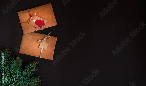 Fototapeta Christmas border on dark background, composed of fresh fir branches and envelope of kraft paper. Merry Christmas and Happy Holidays! Flat lay, top view, copy space.