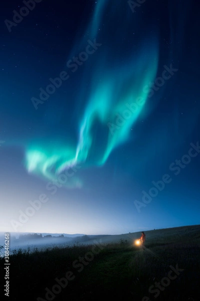 Fototapeta a man with a lantern walking on a field at night with aurora on the sky