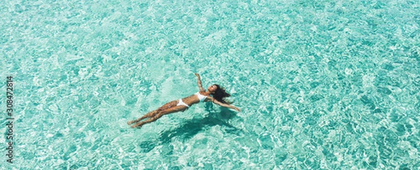 Fototapeta Woman in white bikini lying on transparent turquoise water surface on beach. Travel and vacations concept. Tropical background with empty space