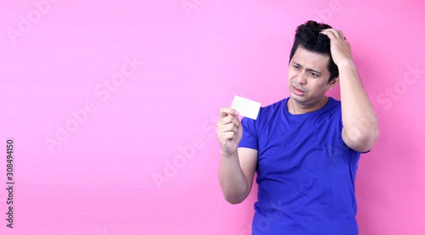 Fototapeta Young handsome  Asia man holding credit card  space scared in shock with a surprise face, afraid and excited with fear expression   on pink background in studio With copy space.