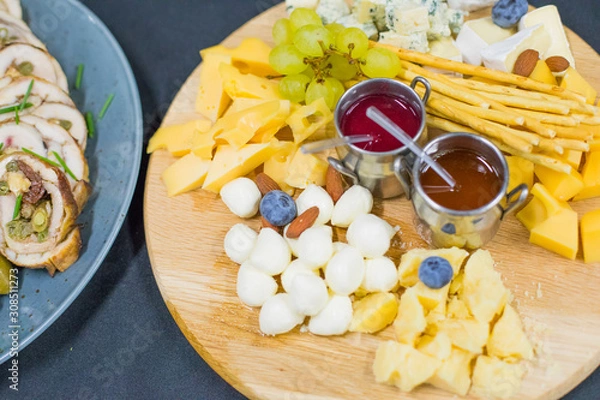 Fototapeta Cheese plate: Parmesan, cheddar, gouda, mozzarella and grapes and berry sauce. Tasty appetizers.  Top view