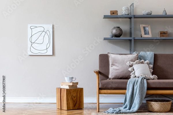 Fototapeta Stylish interior design of living room at cozy apartment with brown sofa, gray bookstand, wooden cube with tea cup and elegant accessories. Mock up poster frames on the wal. Home staging Beige concept