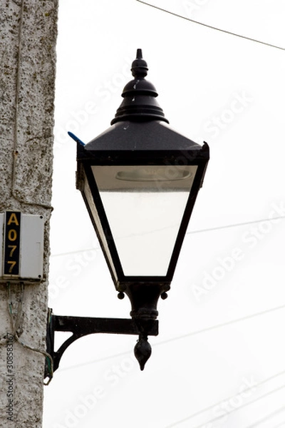 Obraz Very old style english vintage street lamp or gas lamp. victorian design in a black box with glass walls for the light to escape. Mounted on modern architecture wall in the current age