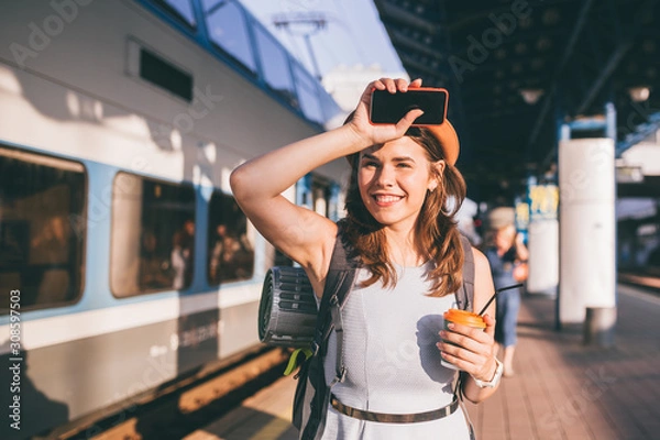 Fototapeta Tourism and travel in the summer. Vacations for the student. Work and travel. Caucasian young woman drinks coffee on the platform of the railway station against the background of the train