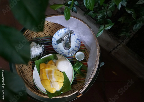 Fototapeta Popular dessert of Thailand: Sticky rice with ripe mango and coconut ball dessert in bamboo basket on green leaves  background, Top view and copy space. 