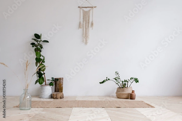 Obraz Wicker rug is lying on wooden floor next to pots with plants and hanging on the wall with wicker macrame on a white background. Concept is a cozy place in the house for classes. Advertising space