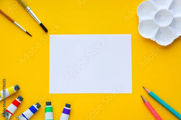 Fototapeta top view of brushes, color tubes, pencils, palette and white paper on yellow background, copy space, flat lay, paintings art concept