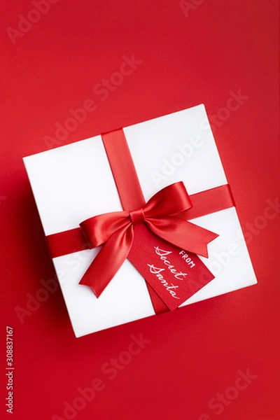 Fototapeta Christmas gift box with red ribbon and a bow from secret Santa on the red background