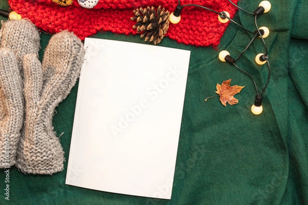 Obraz Christmas mockup, with a postcard, wishes, letter on the blanket with a kettle, leaf, tea, cone, chocolate and xmas tree lights.  Background top view blank space for text.
