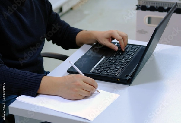 Fototapeta Engineer working on computer and taking some notes on a white paper