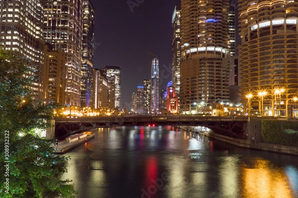 Obraz Night time exterior establishing shot overlooking Chicago river front area with skyline illuminated in dark sky reflecting off water in beautiful scene