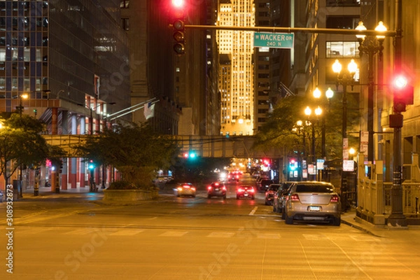 Obraz Night time exterior view of downtown Chicago look down busy street past intersection crosswalk wacker drive cars traveling past skyscraper buildings