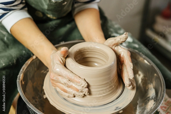 Fototapeta Hands of potter making clay pot on potter's wheel