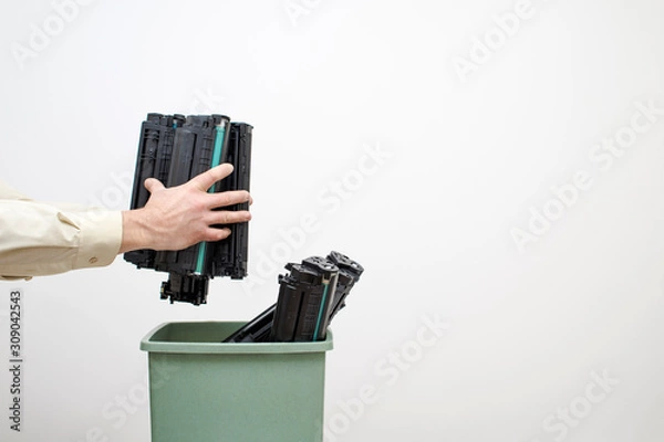 Fototapeta Male hands of an office worker stack spent cartridges in a bucket against a white wall.