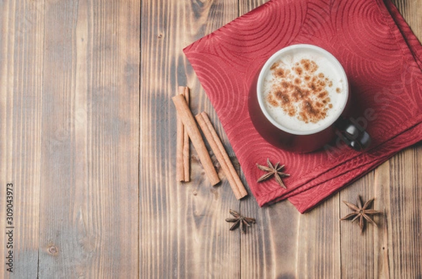 Fototapeta Eggnog. Traditional christmas cocktail in a black mug on a red napkin with cinnamon sticks and anise on wooden table. Top view and copyspace.