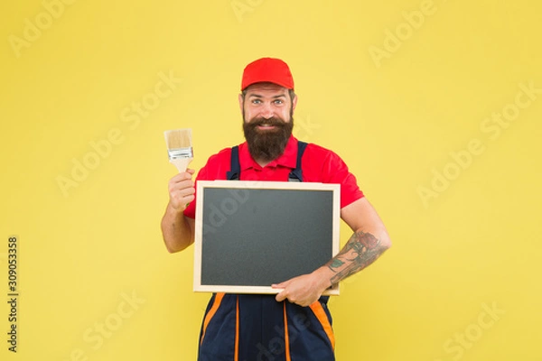 Fototapeta Painting works. Bearded decorator hold blackboard copy space. Repair tips. Happy hours. Man worker with paint brush. Builder regular worker. Repair and renovation. Quick repair. Creative decorator