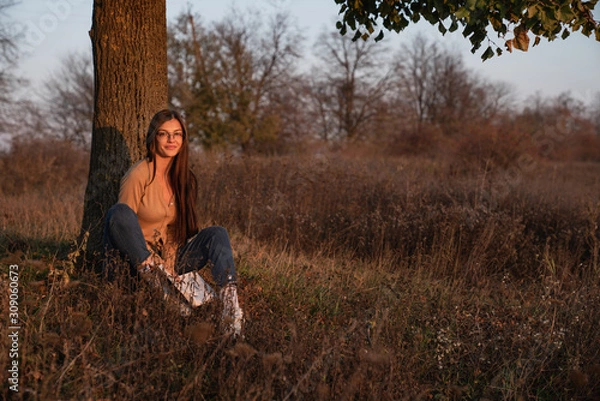 Obraz Student female in casual clothes sitting with book under the tree among the meadow