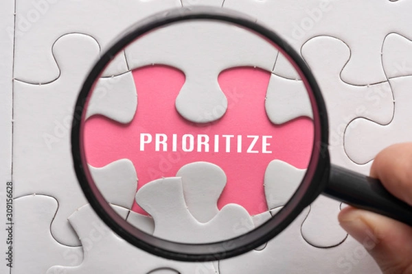 Fototapeta Hand hold magnifying glass with puzzle, focus on the word Prioritize. Business concept.