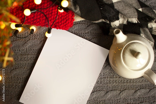 Obraz Christmas mockup, with a postcard, wishes, letter on the blanket with a kettle, leaf, tea, cone, chocolate and xmas tree lights. Background top view blank space for text.