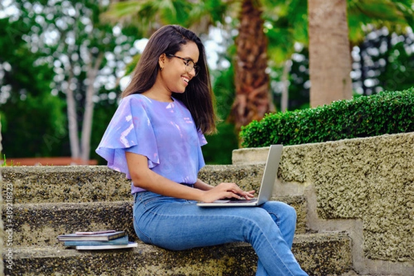 Fototapeta Smiling student girl preparing for exams outdoors with computer