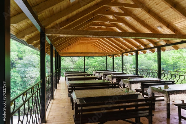 Fototapeta The interior of an open cafe over the river in the mountains. Wooden tables and benches