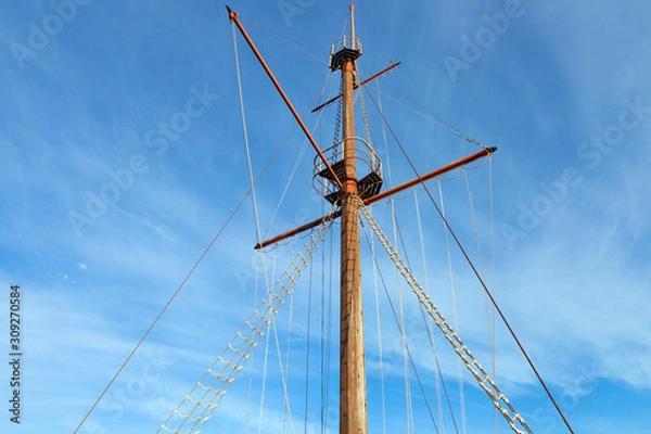 Obraz Wooden top of the old sailing ship mast, yards and rigging against blue sky .