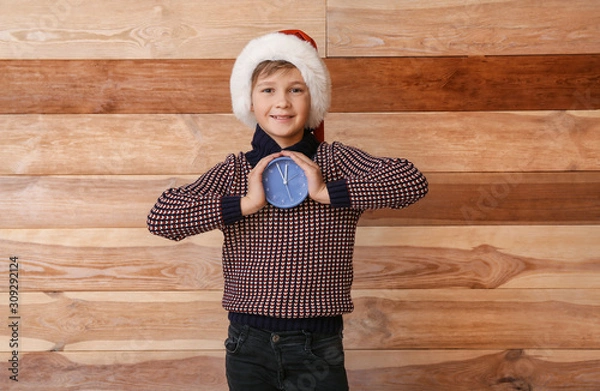 Fototapeta Little boy with alarm clock on wooden background. Christmas countdown concept