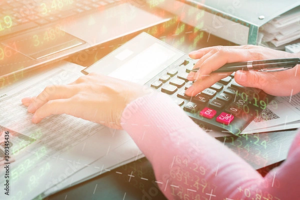 Fototapeta Business woman works at home and counts annual income using a calculator. The remote work, freelance, profit and market analysis concept. Double exposure with digital graphics and a girl in the office