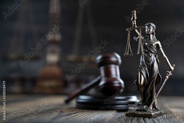 Fototapeta Justice concept. Themis statue and judge's gavel on the rustic wooden table and the dark background.