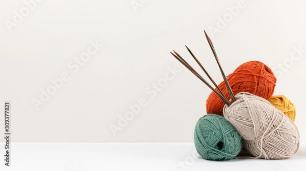 Fototapeta Red, green, yellow and beige pastel colored clews of yarn. Multicolored wooden knitting needles stuck in the ball. Template for your design. Copy space. Female hobby. Needlework and leisure concept.