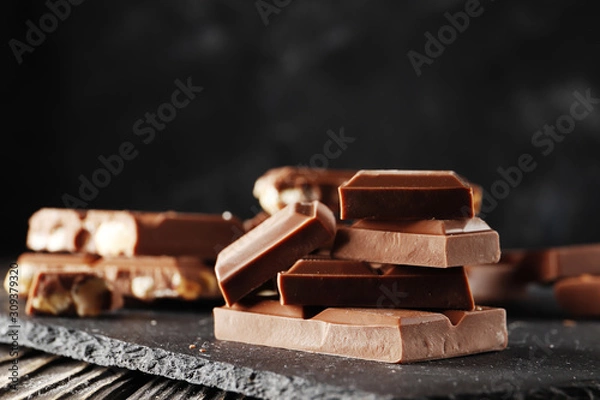 Fototapeta Hazelnut,  and almond, milk and dark chocolate pieces tower  on dark background close-up