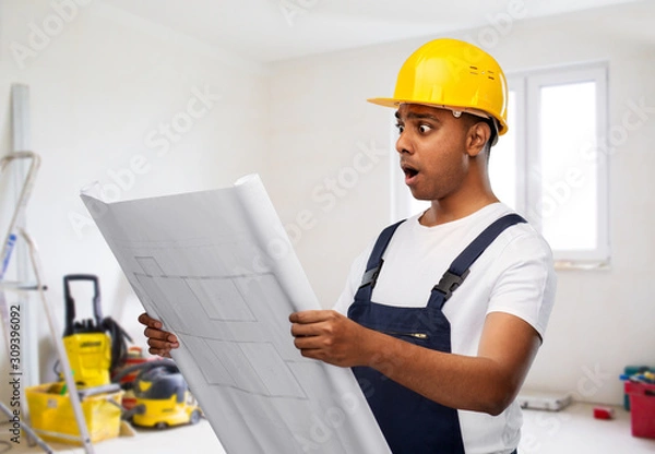 Fototapeta profession, building and repair concept - shocked indian builder or repairman in helmet with blueprint over empty room with construction equipment background