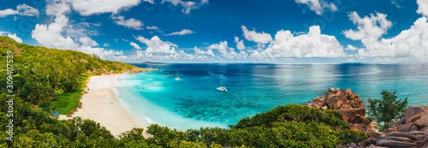 Fototapeta na wymiar Aerial Pano plaży Grand Anse na wyspie La Digue na Seszelach. Biała piaszczysta plaża z błękitną laguną oceaniczną i zacumowanym katamaranem