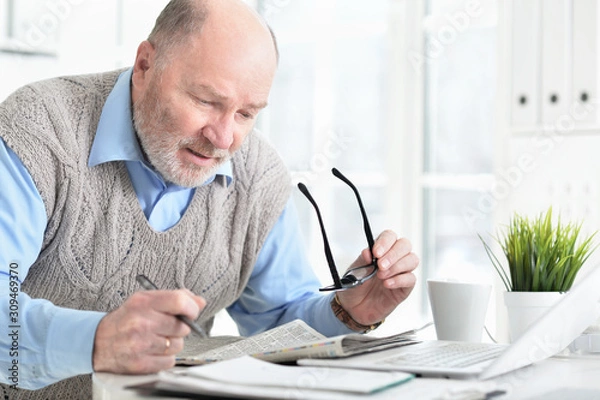 Fototapeta Portrait of emotional senior man reading newspaper at home