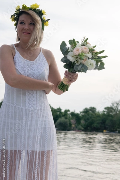 Fototapeta beautiful bride with wedding bouquet standing on a boat and posing for the photographer near the river