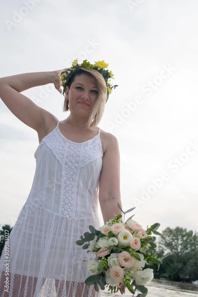 Fototapeta beautiful bride with wedding bouquet standing on a boat and posing for the photographer near the river