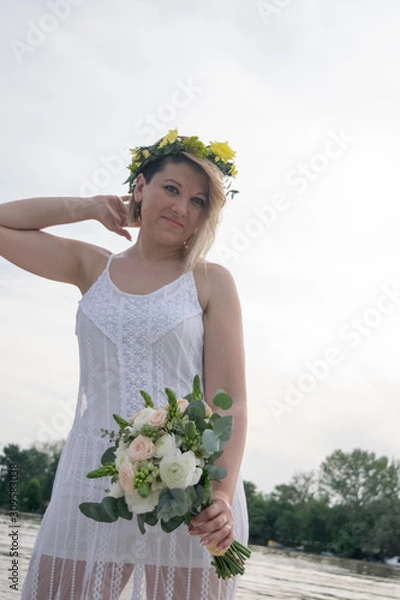 Fototapeta beautiful bride with wedding bouquet standing on a boat and posing for the photographer near the river