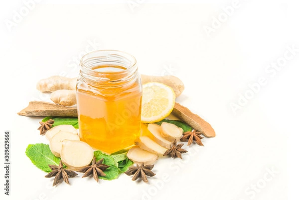 Fototapeta Glass jar of honey and dipper with ginger, mint, carnation, cinnamon and lemon isolated on a white background with space for text 
