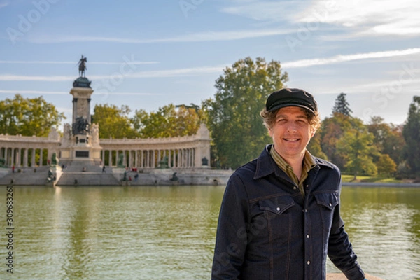 Obraz A father poses for a photo during a family trip to Madrid, in El Retiro park. He laughs and smiles widely.