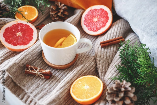 Fototapeta Christmas cozy winter home decor. New year still life: cup of citrus tea, oranges, grapefruits, cinnamon sticks, pine cones, fir branches, knitted sweater.