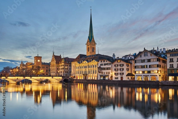 Fototapeta Zürich Altstadt bei Abenddämmerung, Münsterbrücke, Kirchturm Fraumünster und Zunfthaus zur Meisen beleuchtet, Spiegelungen in der Limmat