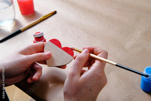 Fototapeta Side view of the female colouring the wooden heart in LGBT pride colours with acrylic paints. Valentine day, masterclass, tutorial, handicraft concept