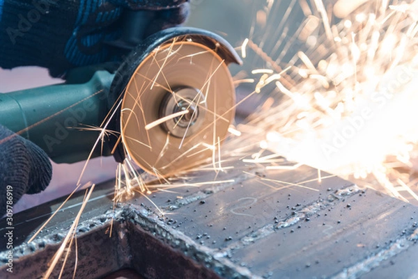 Fototapeta Cut metal with a Angular grinding machine. Sparks are flying. Construction tool grinder. A man is cutting metal. Wear gloves for safety.