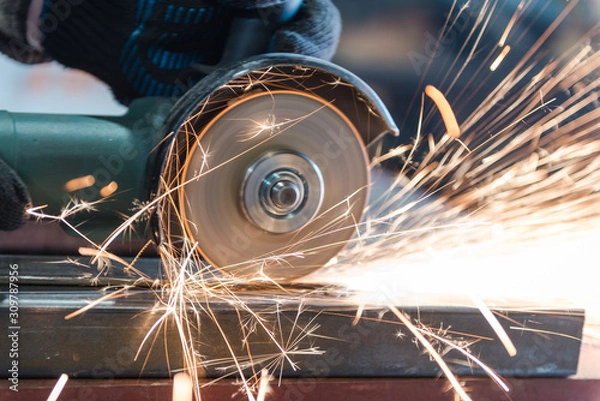 Fototapeta Cut metal with a Angular grinding machine. Sparks are flying. Construction tool grinder. A man is cutting metal. Wear gloves for safety.