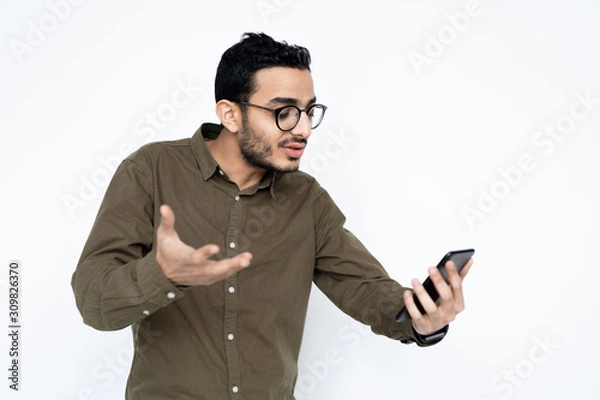 Fototapeta Young anxious businessman looking at screen of smartphone in front of himself